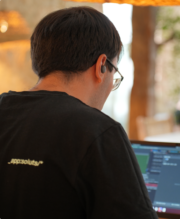 Rückansicht einer Person mit appsoluts-Shirt, die konzentriert am Laptop arbeitet.